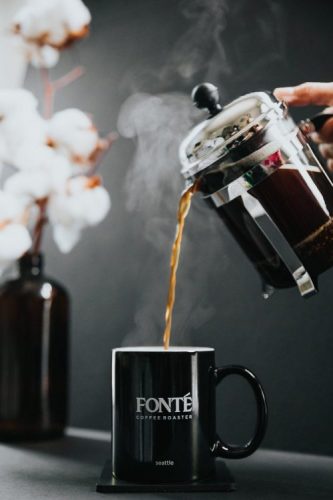 french press pouring into coffee cup, flower in background
